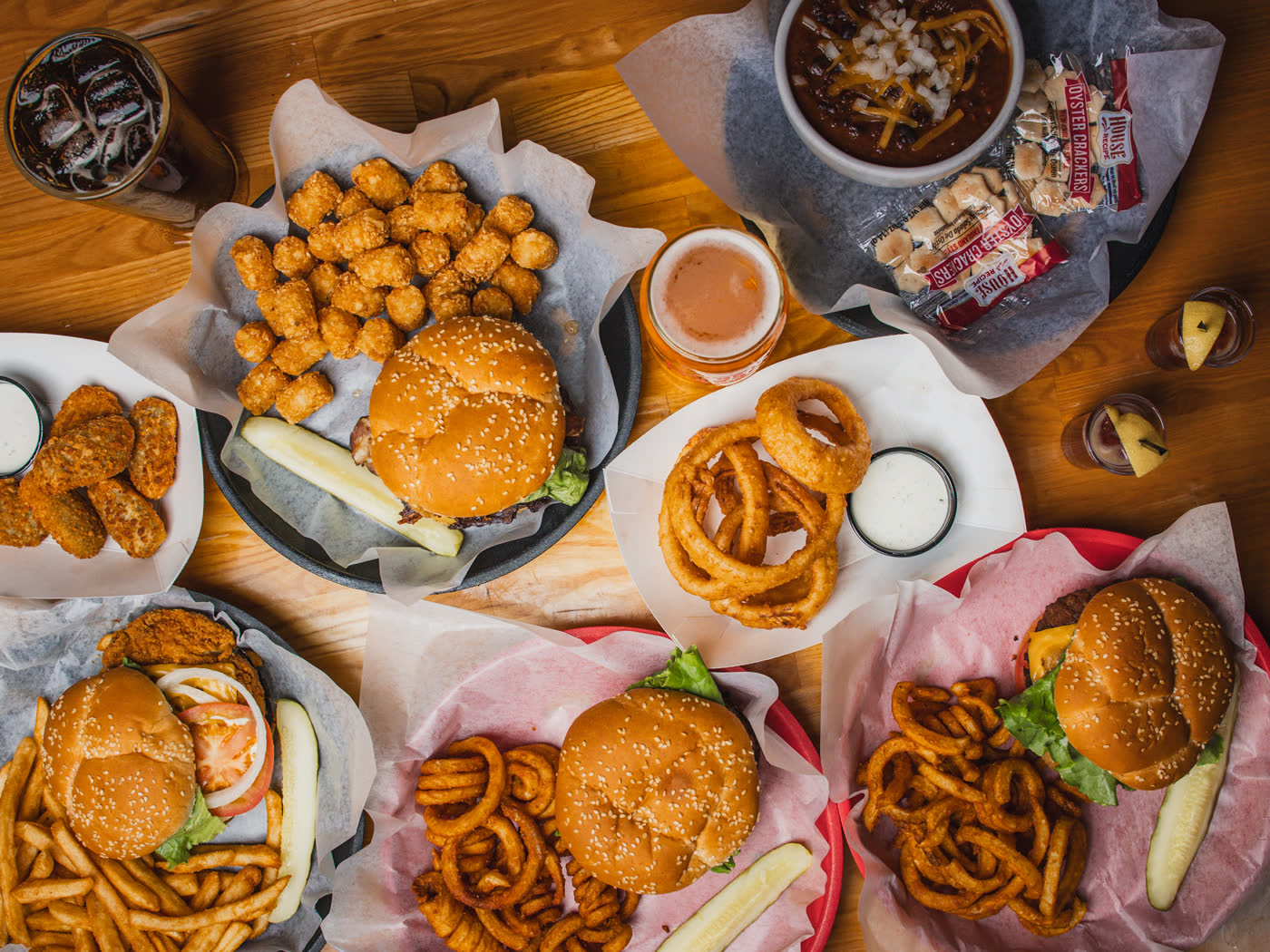 Overhead table spread of burgers, curly fries, tater tots, onion rings, chili and beer at The Barge Inn Tavern in Newport, Oregon